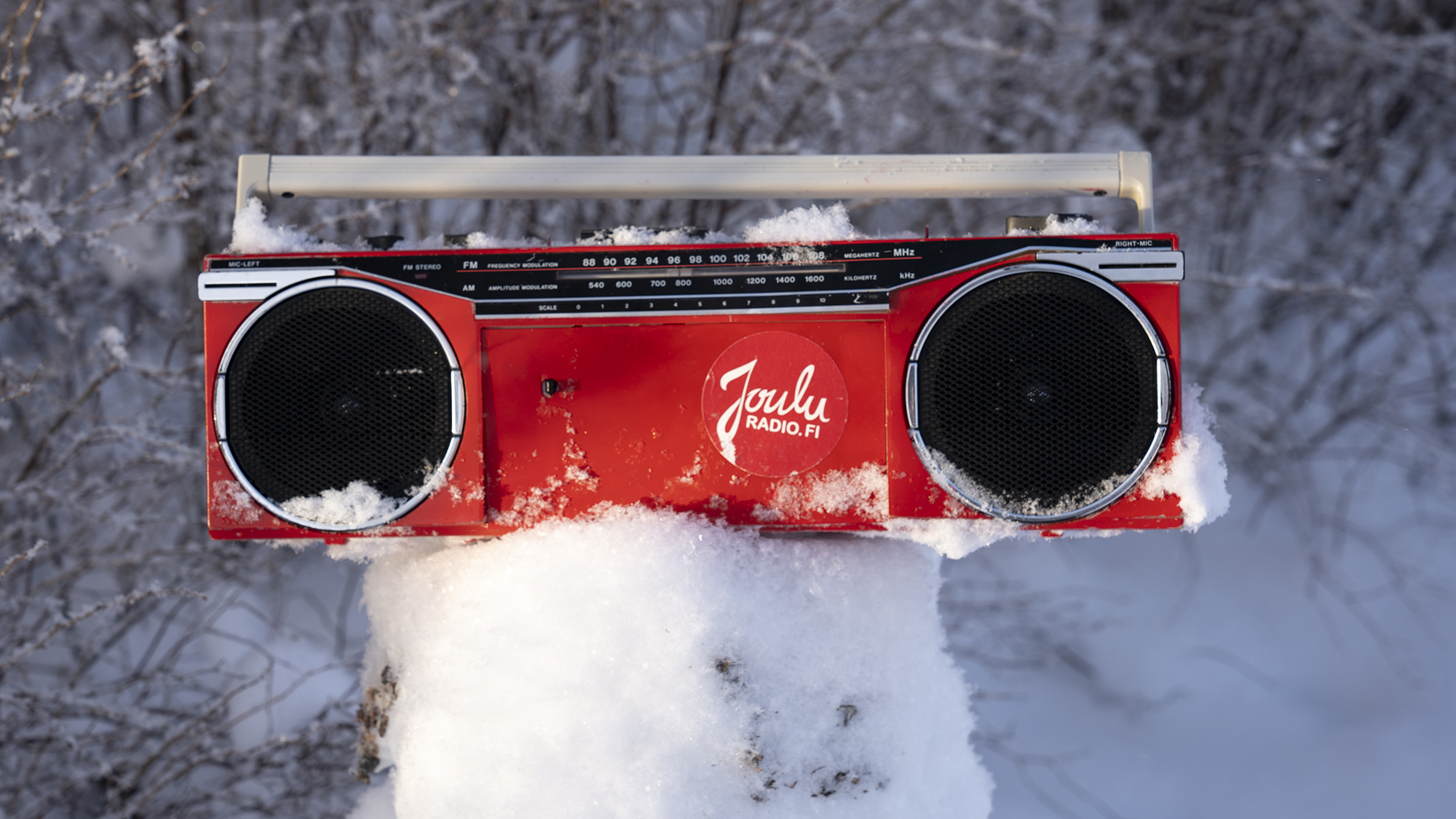 Punainen radio on puunkannon päällä keskellä lumista maisemaa.