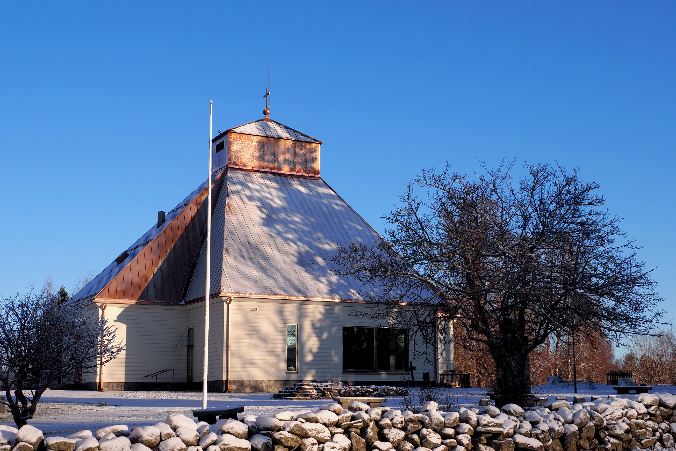 Puinen kirkkorakennus lumisessa maisemassa, etualalla kiviaita.