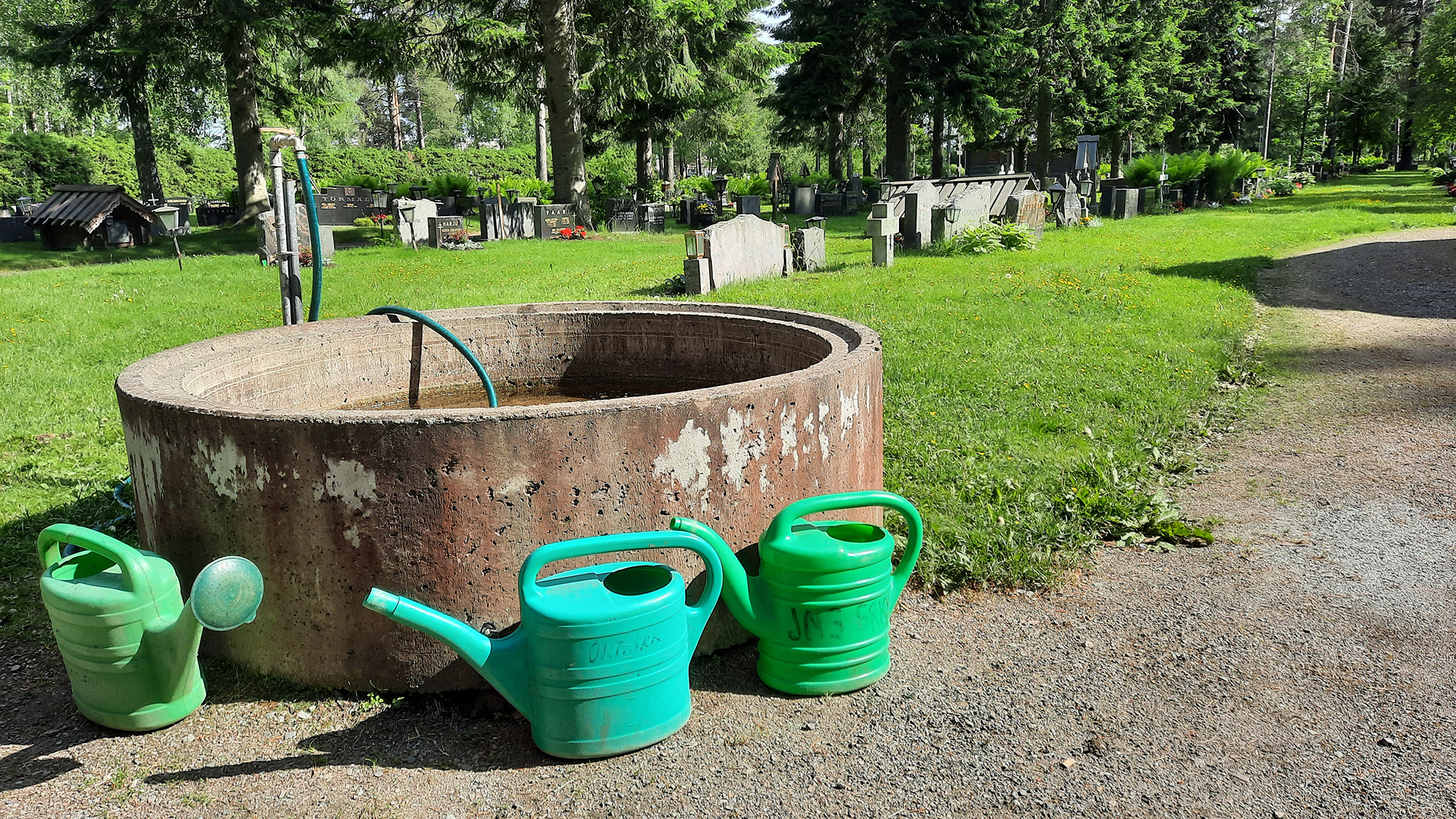 Vihreitä kastelukannuja vesialtaan luona hautausmaalla.