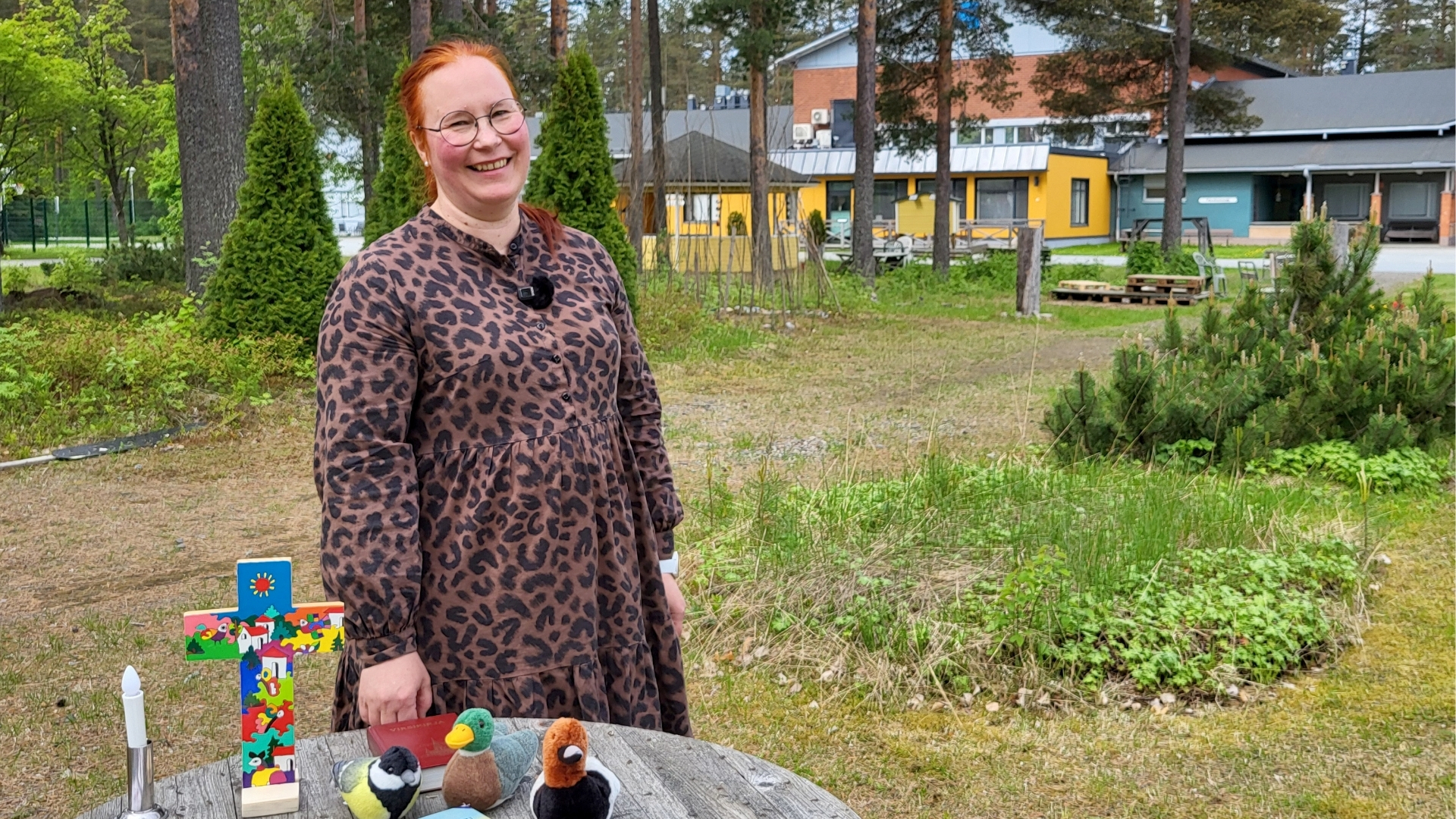 Minna Snellman ulkona kesällä edessään pöytä, jolla erilaisia esineitä.
