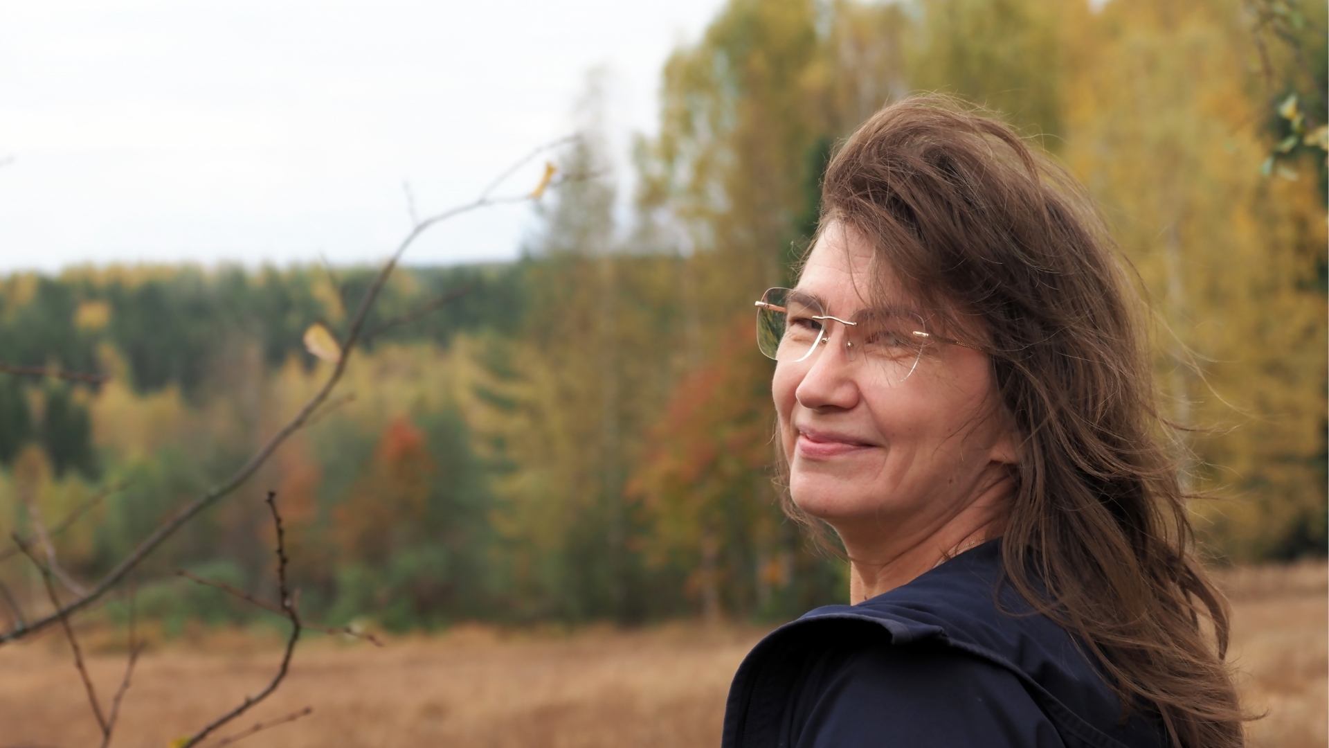 Suvi Luopakka katsoo olan yli kameraan syksyisessä maalaismaisemassa.