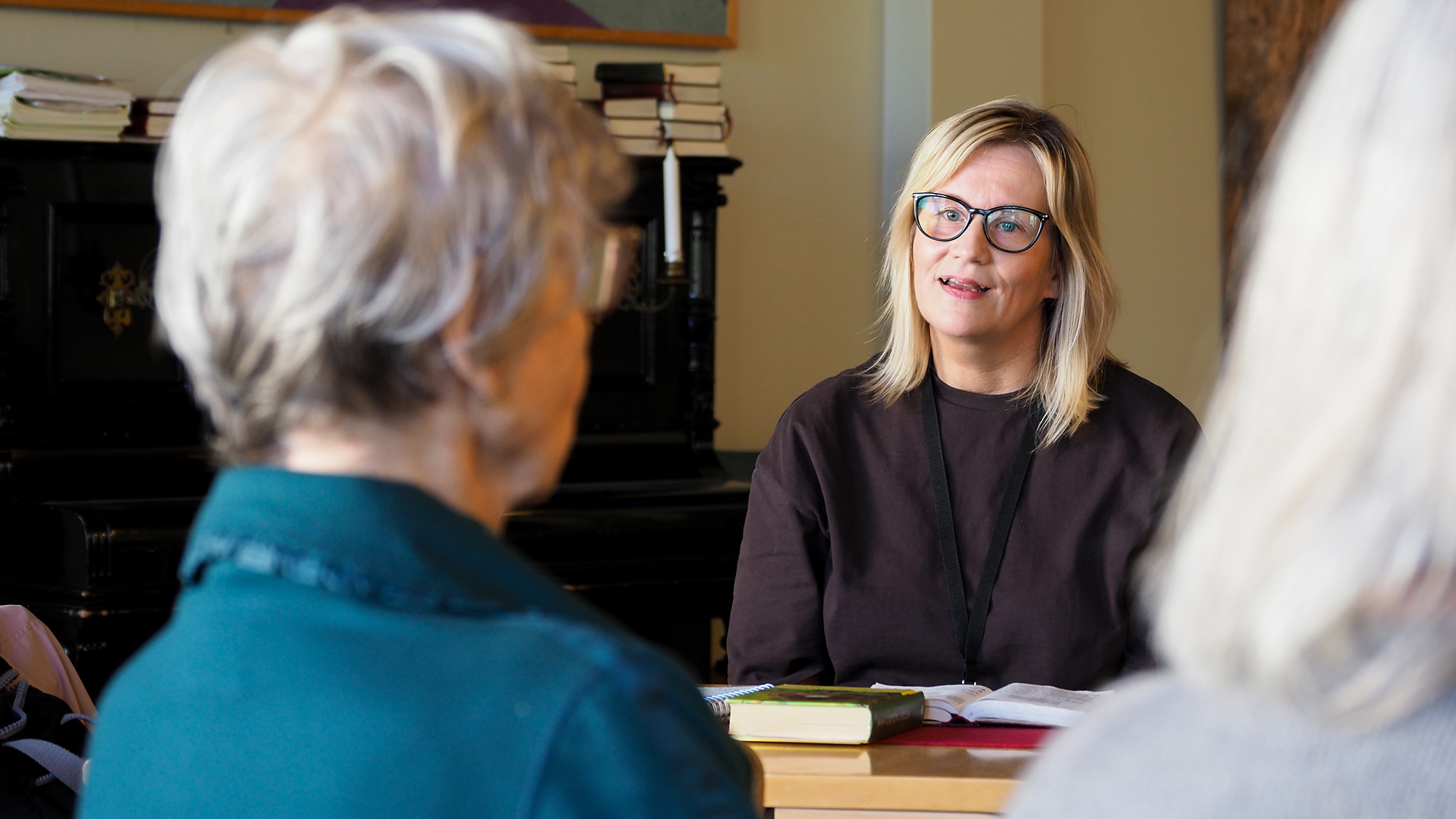 Heli Solonen istuu ja puhuu. Etualalla näkyy vanhusten päitä.