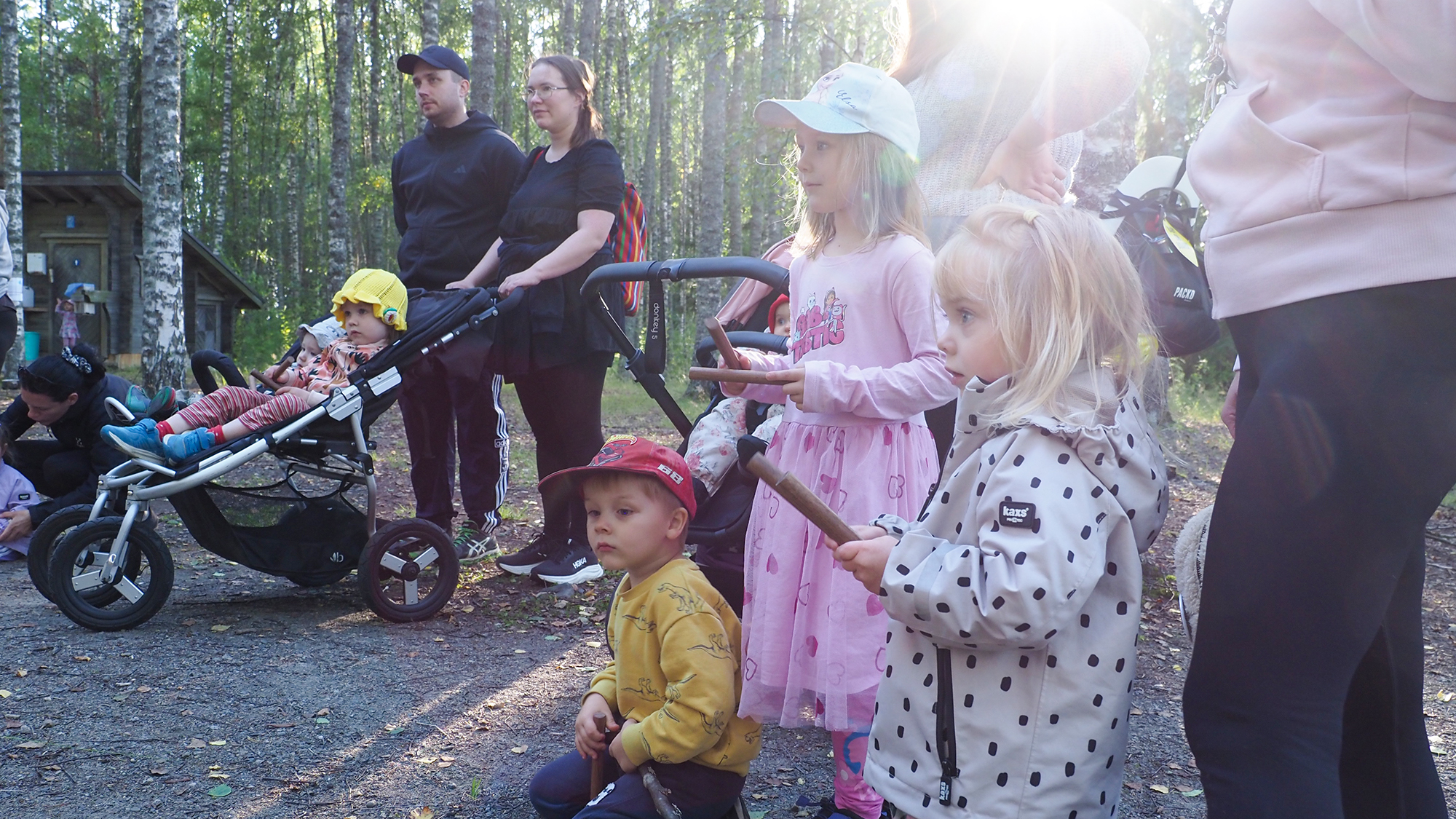 Lapsilla on käsissään rytmikapulat. Taustalla näkyy metsää ja auringonvaloa.