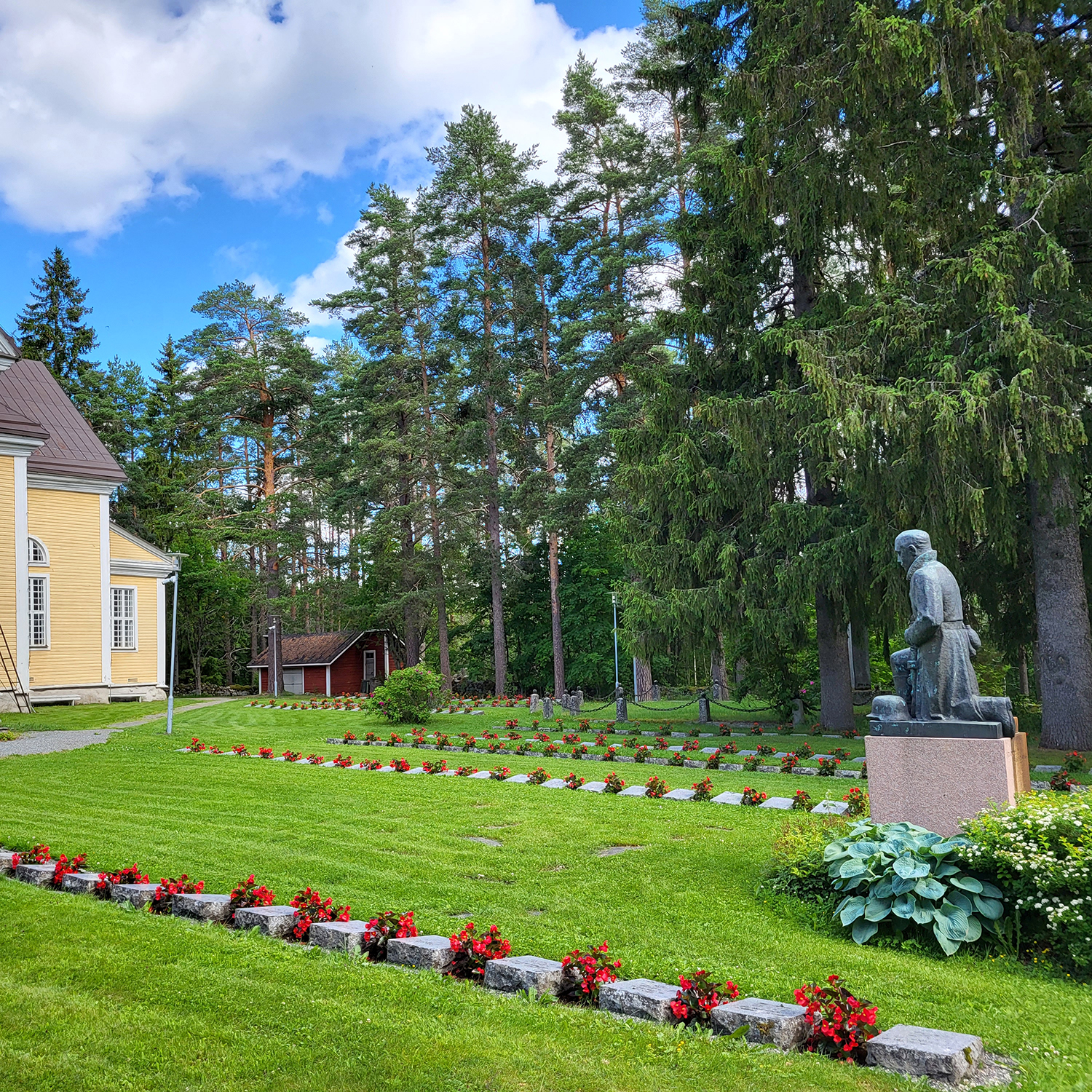 Hauta-alue kirkkopihalla, muistokiviä, sotilaspatsas.