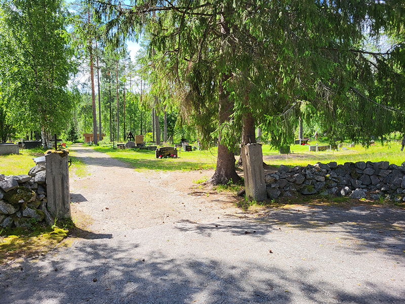 Hautausmaa-alue taustalla, etuosassa kivinen aita ja portinpielet.