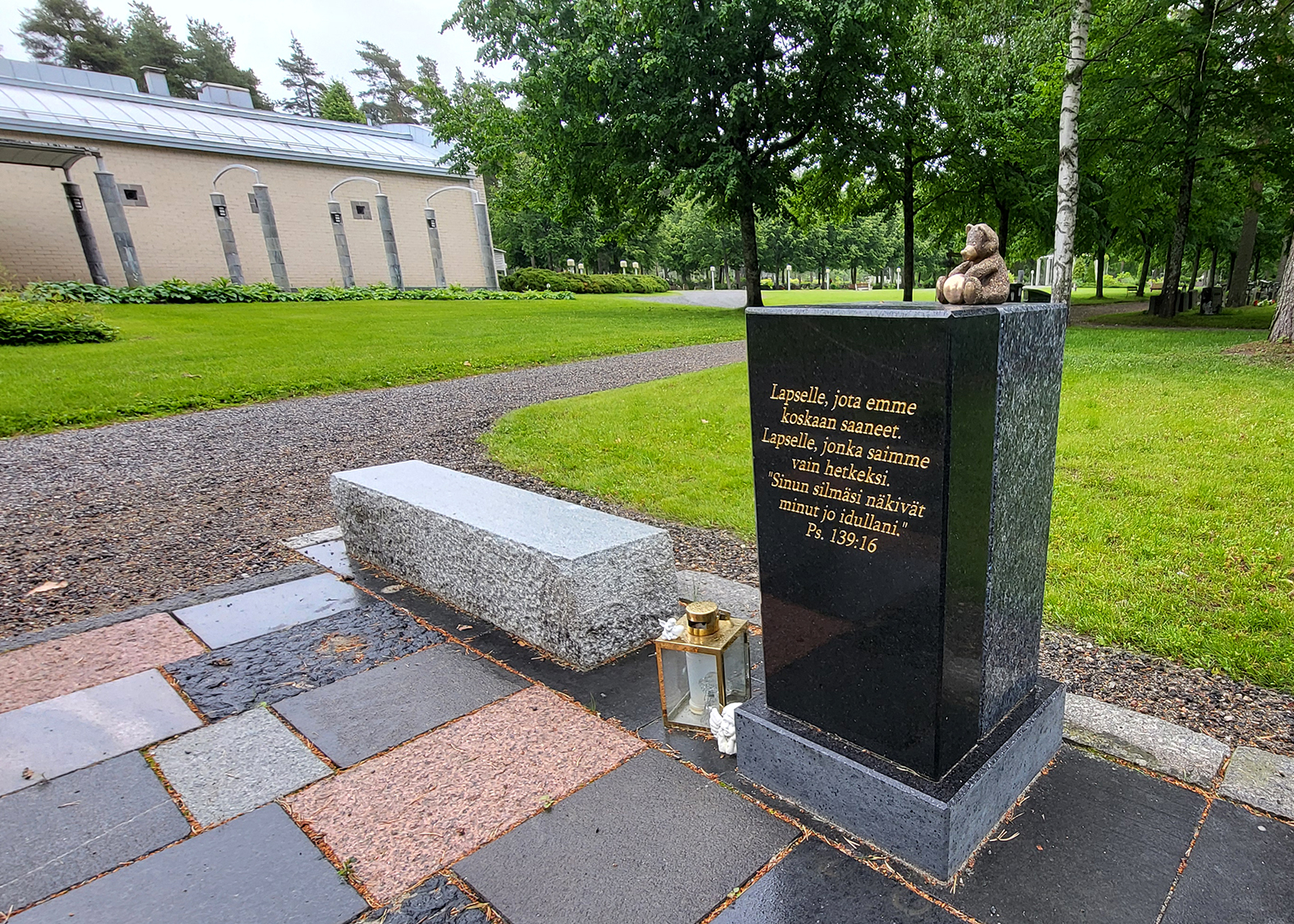 Tyhjän sylin muistopaikka Hautausmaa-alue taustalla, etualalla kivetty alue, jossa muistomerkki.