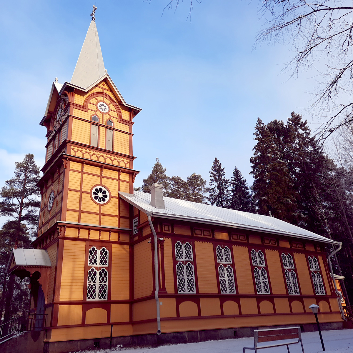 Kelta-ruskea vanha puukirkko, etuosassa torni, koristeelliset ikkunat.