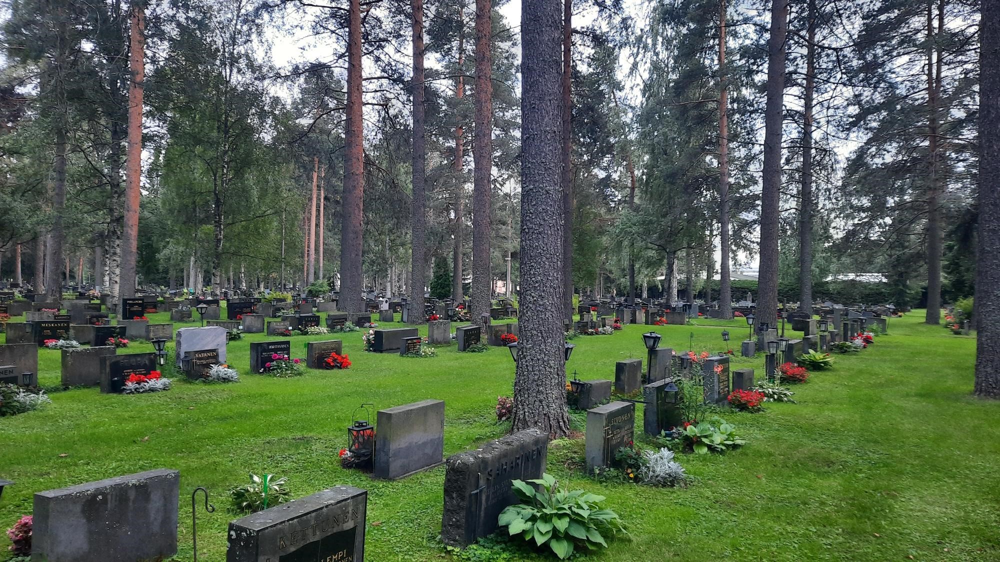 maisema kesäiseltä hautausmaalta, jossa puita ja hautamuistomerkkejä