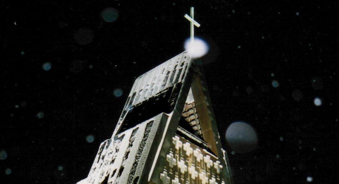 Pielisensuun kirkon torni kuvattuna pimeää taivasta vasten, etualalla sataa lunta.