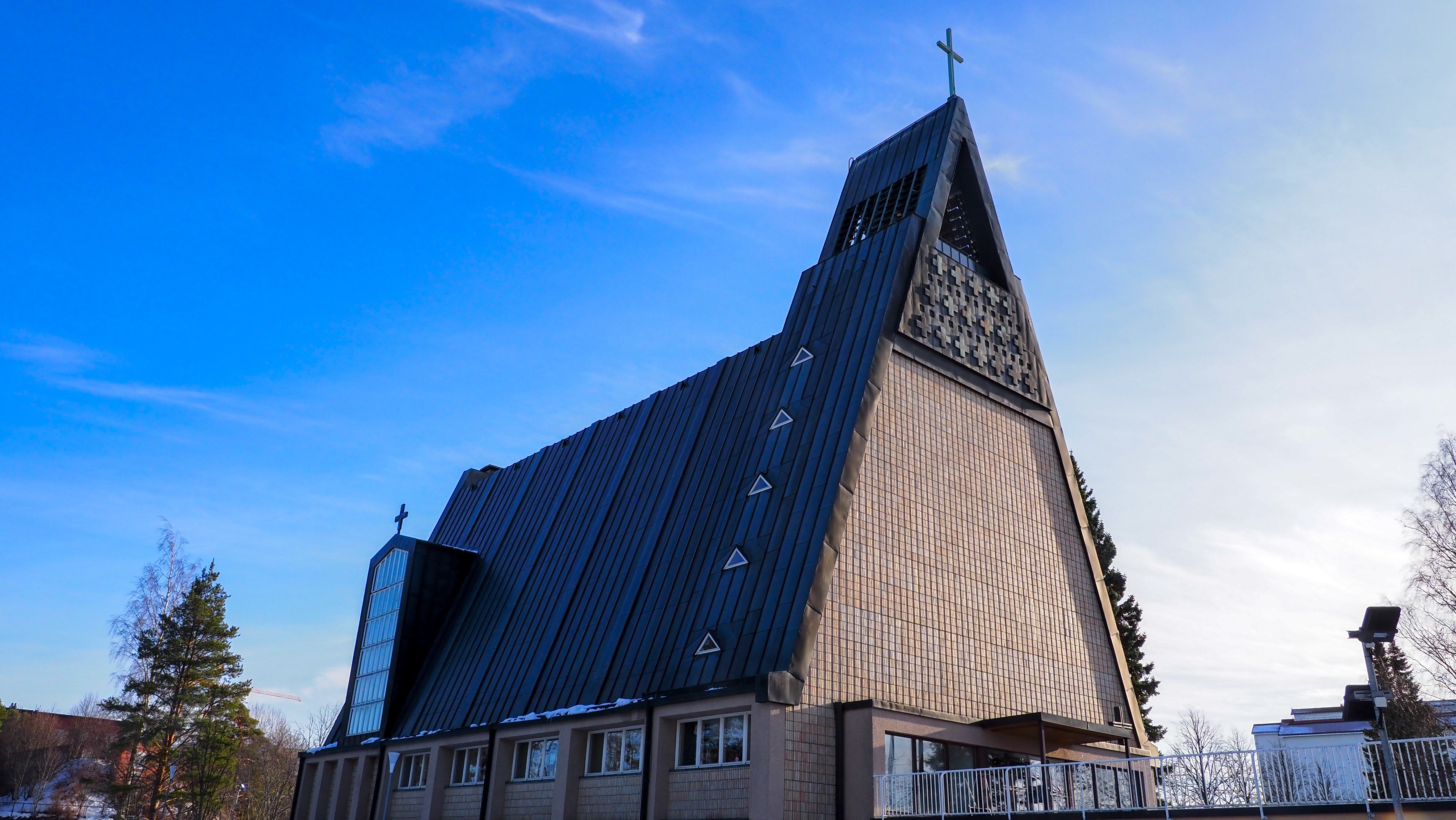 Tiilinen kirkkorakennus, jossa jyrkkä harjakatto, taustalla sininen taivas.