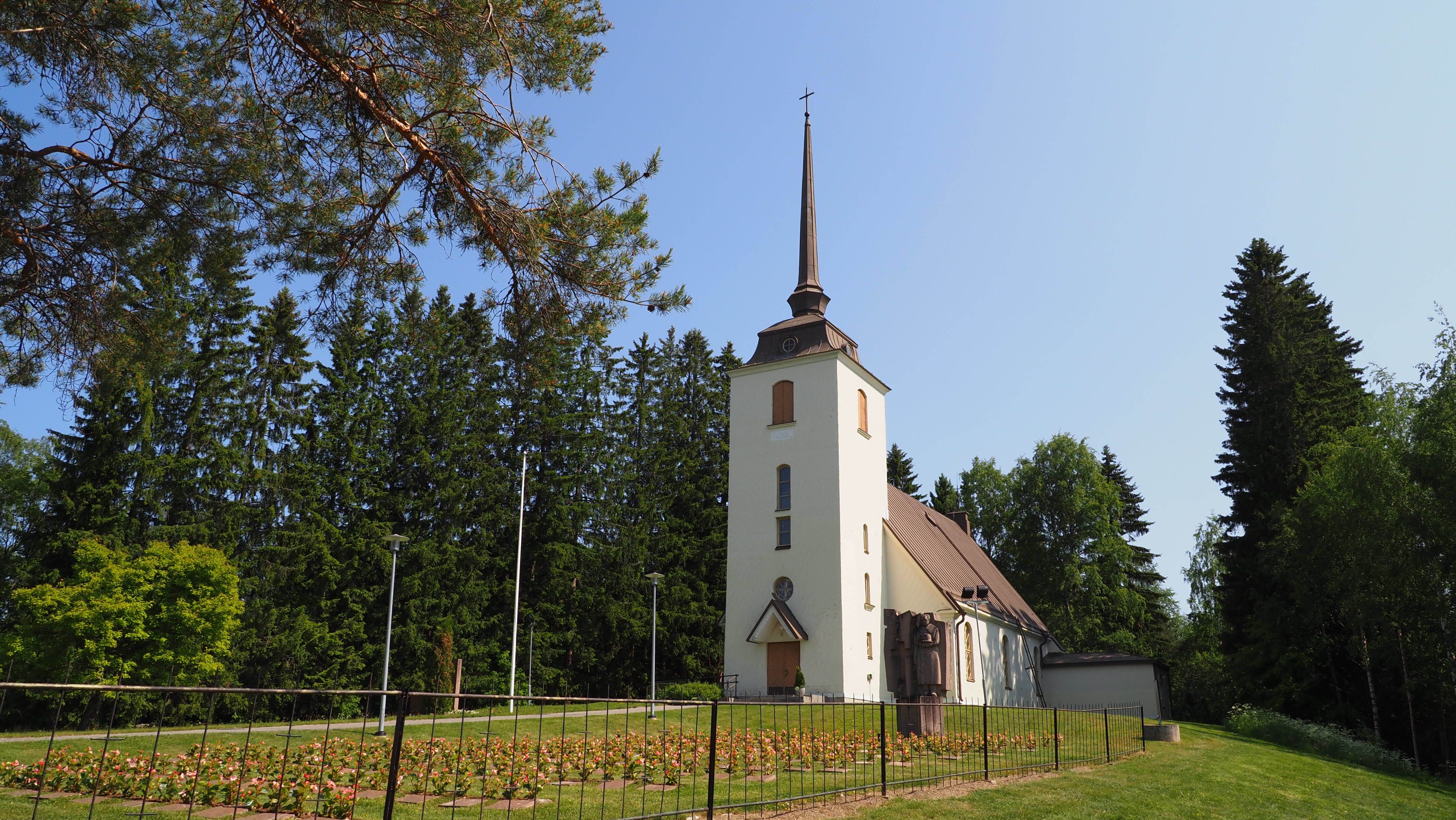 Valkoinen kivinen kirkkorakennus kesäisessä maisemassa.