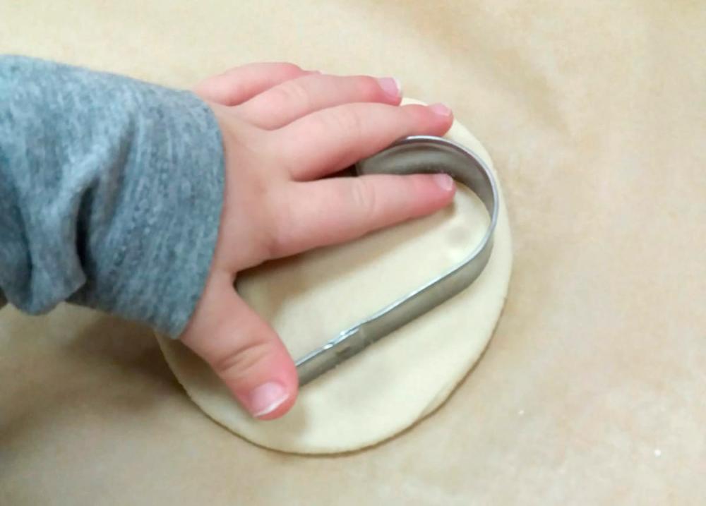 Pienen lapsen käsi painamassa sydämenmuotoisella muotilla taikinaa.