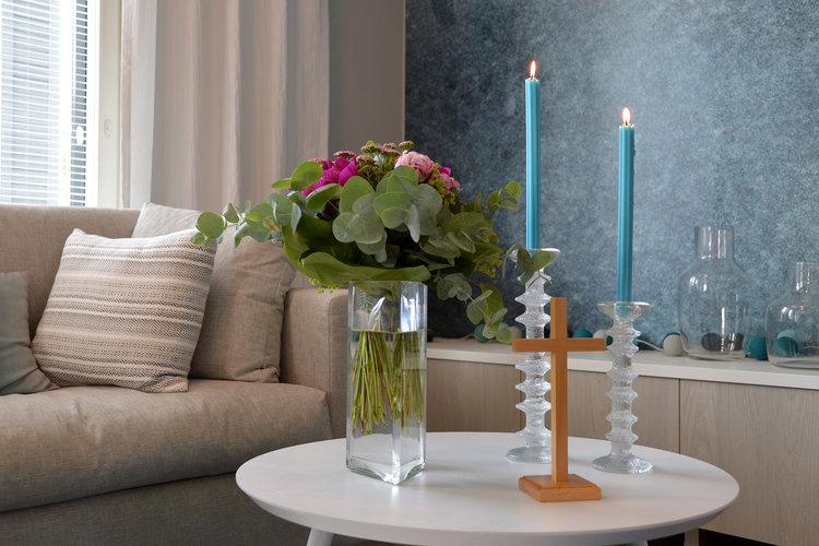 Olohuoneessa oleva siunauspöytä, jolla kukkakimppu, kaksi palavaa kynttilää ja puinen risti.