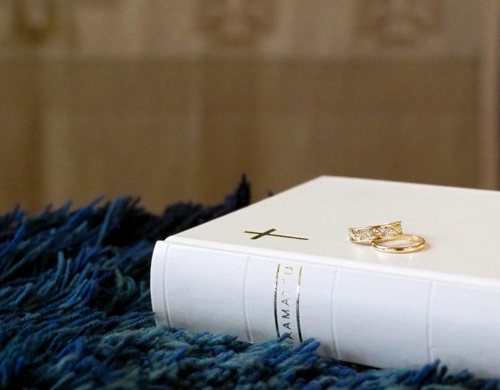 Valkoinen raamattu sinisen ryijyn päällä, kihlasormukset raamatun päällä.
