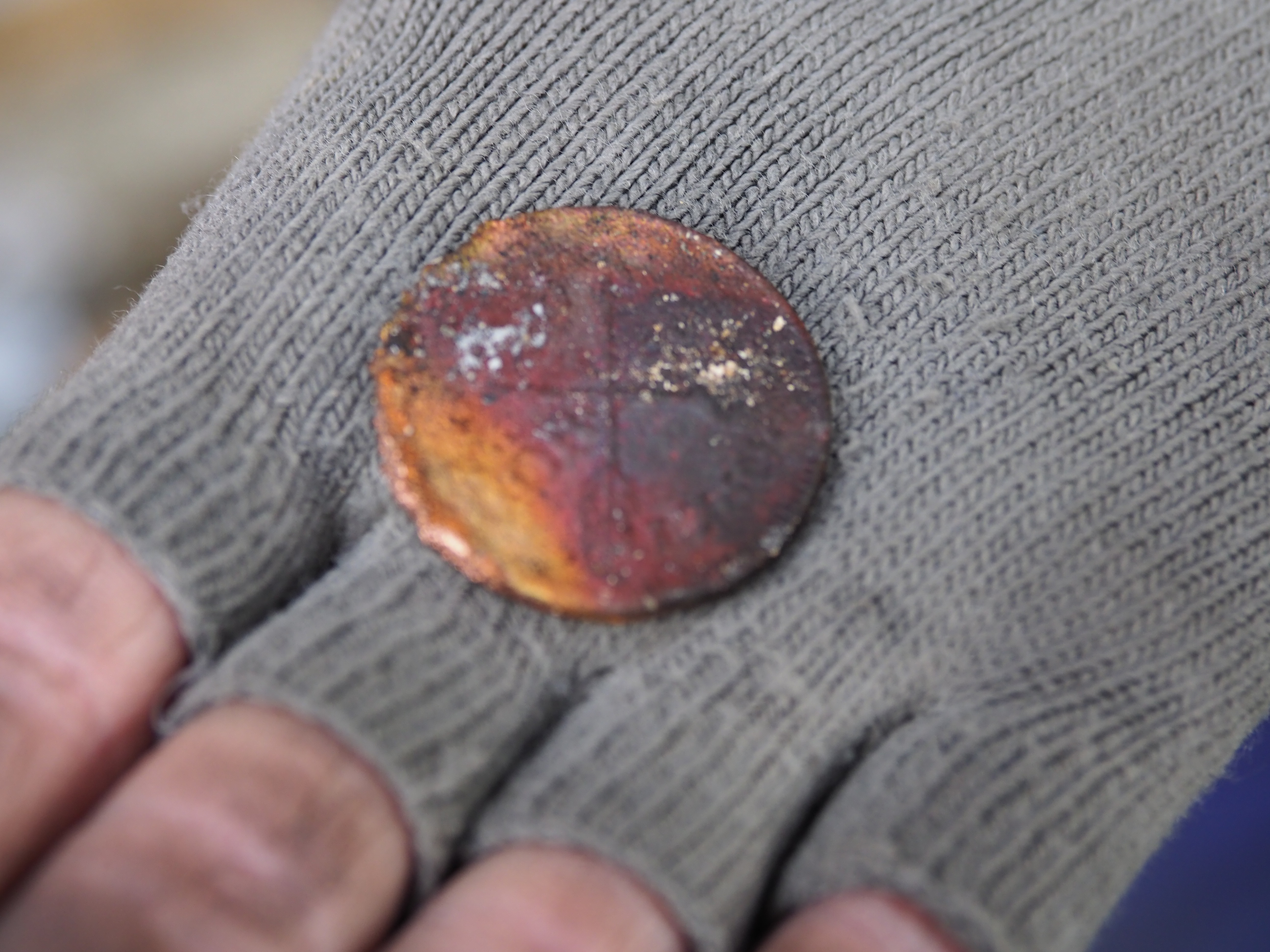 Raunioista löytynyt vanha kolikko arkeologin kädessä.
