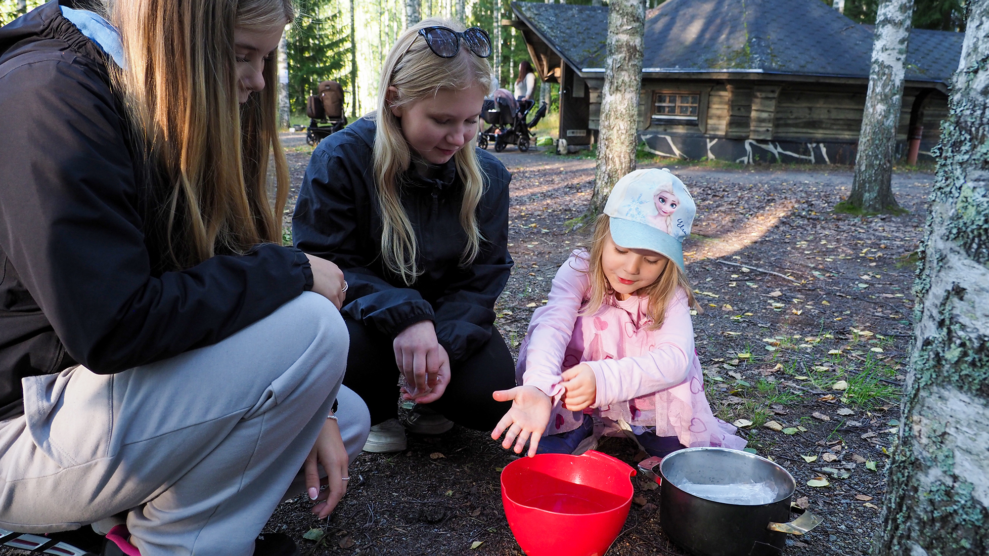 Sofianna Ruohola, Salme Summanen ja Janni Sormunen ovat kyykistyneet muovikulhon ja kattilan viereen.